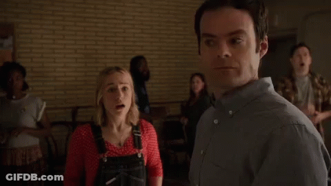A Woman In Overalls Is Standing Next To A Man In A Room . GIF