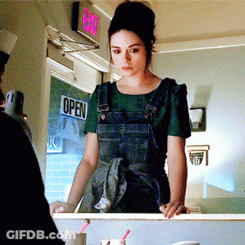 A Woman In Overalls Stands In Front Of A Sign That Says Open GIF