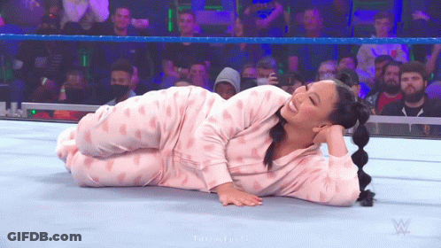 A Woman In Pink Pajamas Is Laying On The Ground In A Wrestling Ring . GIF