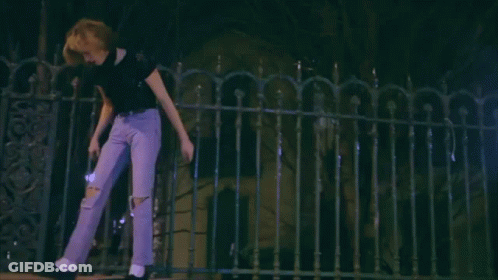 A Woman In Purple Jeans Is Walking Across A Fence At Night GIF