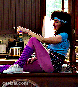 A Woman In Purple Leg Warmers Is Sitting On A Counter GIF