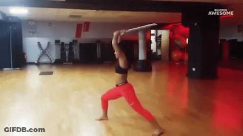 A Woman In Red Pants Is Holding A Sword In A Gym With The Words Awesome On The Bottom GIF