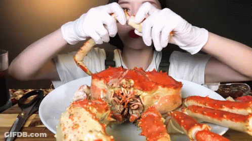 A Woman In White Gloves Is Eating A Large Red Crab GIF