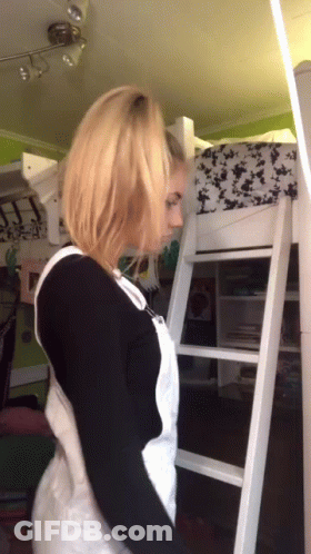 A Woman In White Overalls Is Standing Next To A White Ladder GIF
