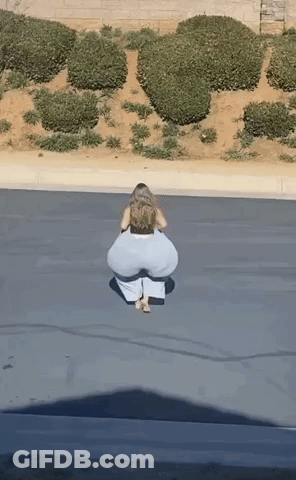 A Woman In White Pants Is Squatting Down On The Side Of The Road GIF