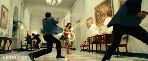 A Woman In Wonder Woman 'S Costume Is Surrounded By Men In Suits GIF