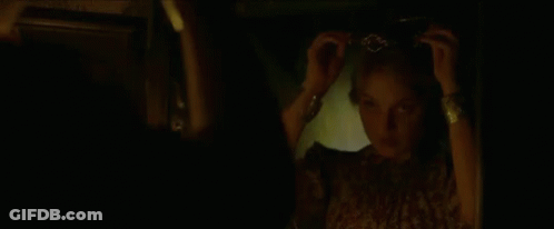 A Woman Is Adjusting Her Hair In Front Of A Mirror In The Dark . GIF