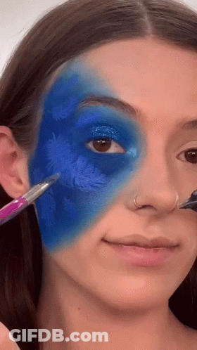 A Woman Is Applying Blue Paint To Her Face With A Brush . GIF
