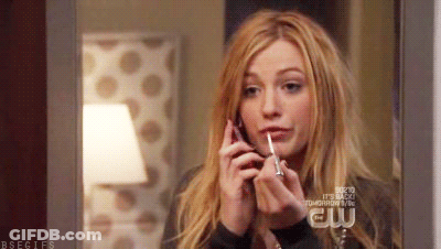 A Woman Is Applying Lip Gloss While Talking On A Cell Phone .. GIF