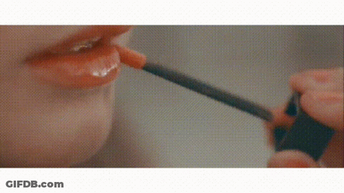 A Woman Is Applying Lip Gloss With A Brush To Her Lips . GIF