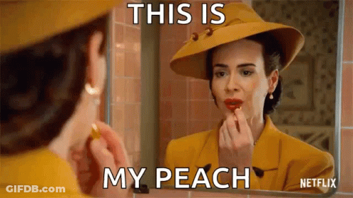 A Woman Is Applying Lipstick In Front Of A Mirror While Wearing A Yellow Hat . GIF