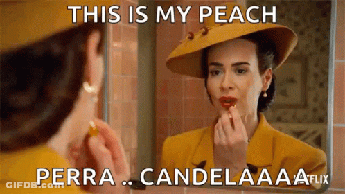 A Woman Is Applying Lipstick In Front Of A Mirror While Wearing A Yellow Suit And Hat . GIF