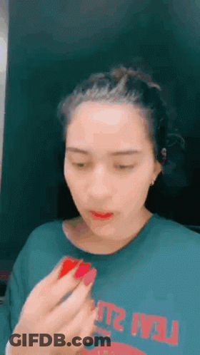 A Woman Is Applying Lipstick To Her Lips While Wearing A Green T-Shirt . GIF