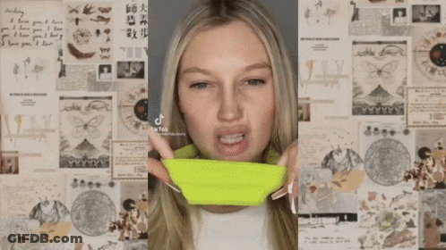 A Woman Is Applying Makeup To Her Face In Front Of A Wall Of Papers . GIF