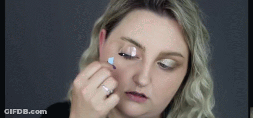 A Woman Is Applying Mascara To Her Eyelashes With A Brush . GIF