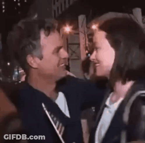 A Woman Is Being Hugged By A Man In A Crowd . GIF