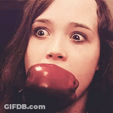 A Woman Is Biting Into A Red Apple With Her Eyes Wide Open GIF