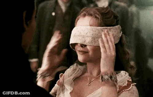 A Woman Is Blindfolded And Smiling While A Man Holds Her Hand Over Her Eyes . GIF