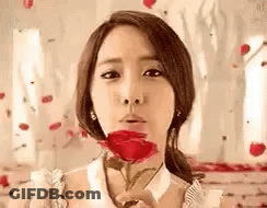 A Woman Is Blowing A Kiss While Holding A Red Rose . GIF