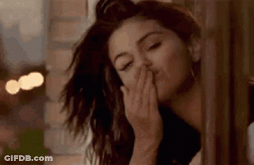 A Woman Is Blowing A Kiss While Standing Next To A Window . GIF