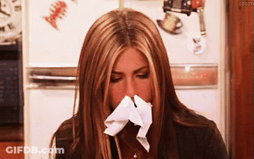 A Woman Is Blowing Her Nose With A Napkin While Sitting In Front Of A Refrigerator . GIF