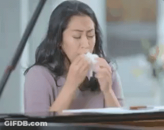 A Woman Is Blowing Her Nose With A Tissue While Sitting At A Piano . GIF