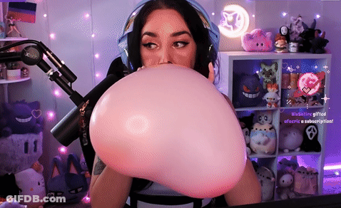 A Woman Is Blowing Up A Pink Balloon In Front Of A Microphone .. GIF