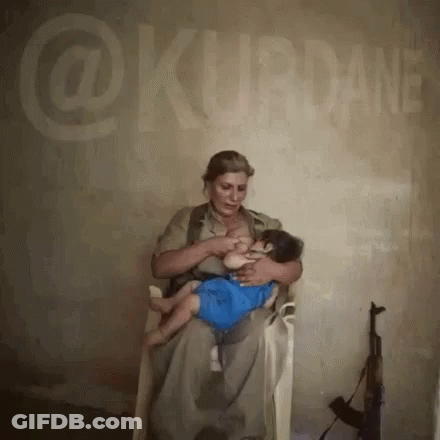 A Woman Is Breastfeeding A Baby While Sitting In Front Of A Wall That Says @Kurdane GIF