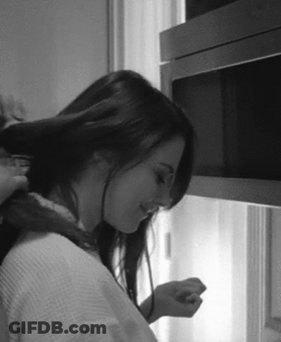 A Woman Is Brushing Her Hair In A Black And White Photo While Standing In Front Of A Microwave . GIF
