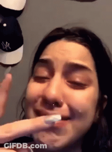 A Woman Is Brushing Her Teeth With A Toothbrush While Holding Her Finger To Her Mouth . GIF