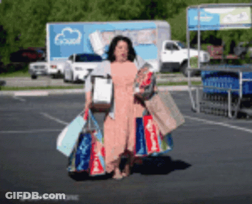 A Woman Is Carrying Shopping Bags In A Parking Lot GIF