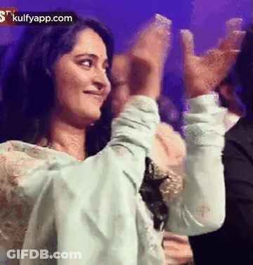 A Woman Is Clapping Her Hands In The Air While Standing Next To A Man . GIF
