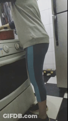 A Woman Is Cooking On A Stove In A Kitchen With A Refrigerator In The Background GIF