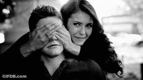 A Woman Is Covering A Man 'S Eyes With Her Hands . GIF