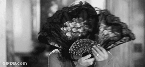 A Woman Is Covering Her Face With A Fan . GIF