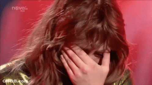 A Woman Is Covering Her Face With Her Hand While Standing On A Stage . GIF