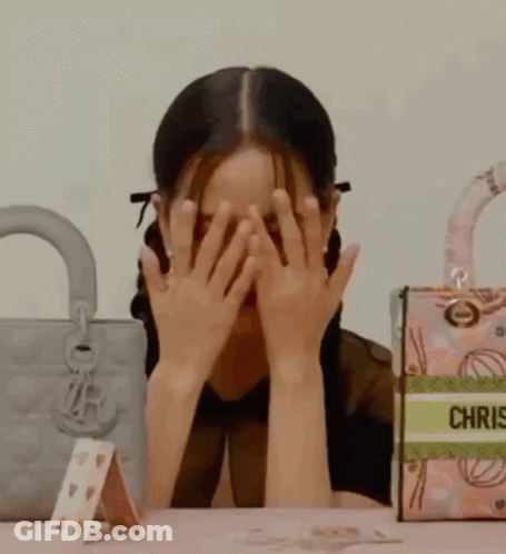 A Woman Is Covering Her Face With Her Hands While Sitting At A Table With Handbags . GIF