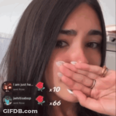 A Woman Is Covering Her Mouth With Her Hand And A Few Roses Are Visible In The Background GIF