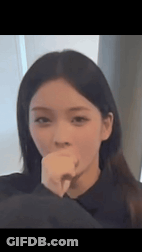 A Woman Is Covering Her Mouth With Her Hand And Looking At The Camera . GIF