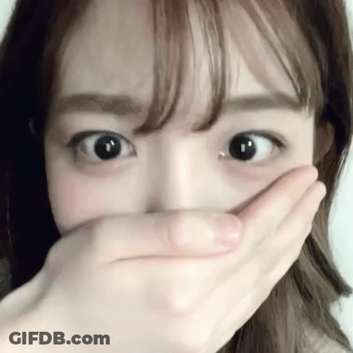 A Woman Is Covering Her Mouth With Her Hand And Looking At The Camera . GIF