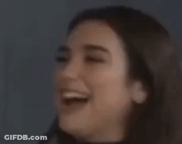 A Woman Is Covering Her Mouth With Her Hand And Looking At The Camera . GIF