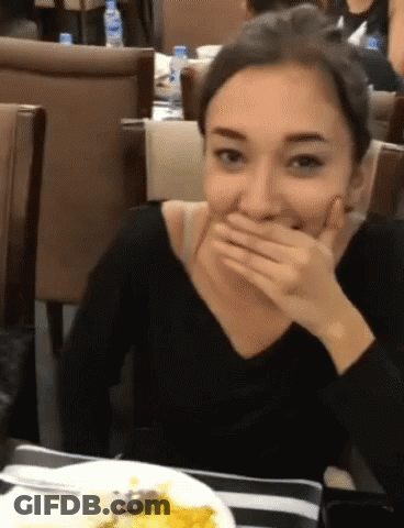 A Woman Is Covering Her Mouth With Her Hand While Sitting At A Table GIF