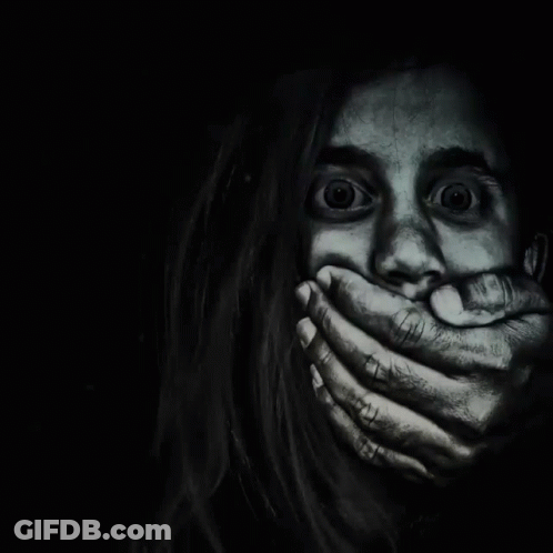 A Woman Is Covering Her Mouth With Her Hands In The Dark GIF