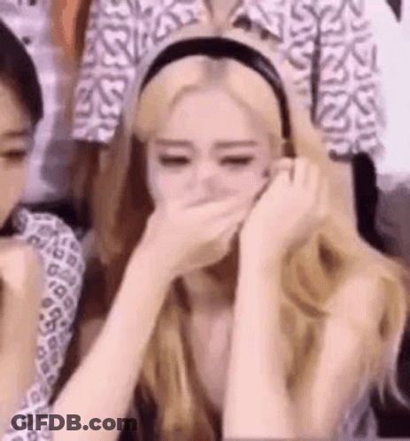 A Woman Is Covering Her Mouth With Her Hands While Sitting In Front Of A Crowd . GIF