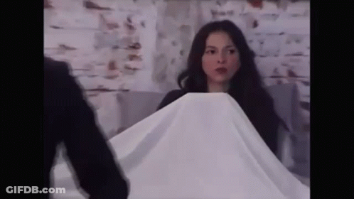 A Woman Is Covering Herself With A White Cloth While A Man Stands Behind Her . GIF