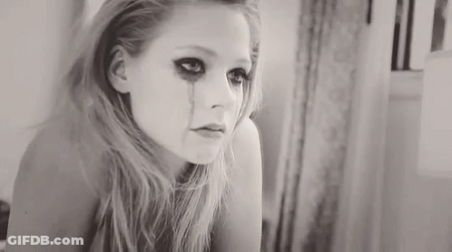 A Woman Is Crying In Front Of A Mirror And Has A Tear Running Down Her Face . GIF