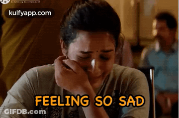 A Woman Is Crying While Sitting At A Table With The Words `` Feeling So Sad '' Written Above Her . GIF