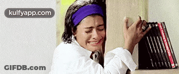 A Woman Is Crying While Standing Next To A Bookshelf . GIF