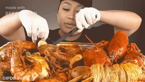A Woman Is Cutting A Lobster With A Pair Of Scissors In Front Of A Tray Of Seafood GIF