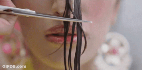 A Woman Is Cutting Her Hair With Scissors In Front Of Her Face GIF